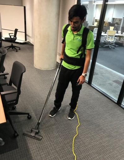 Professional office cleaner vacuuming carpeted floor in a modern workplace